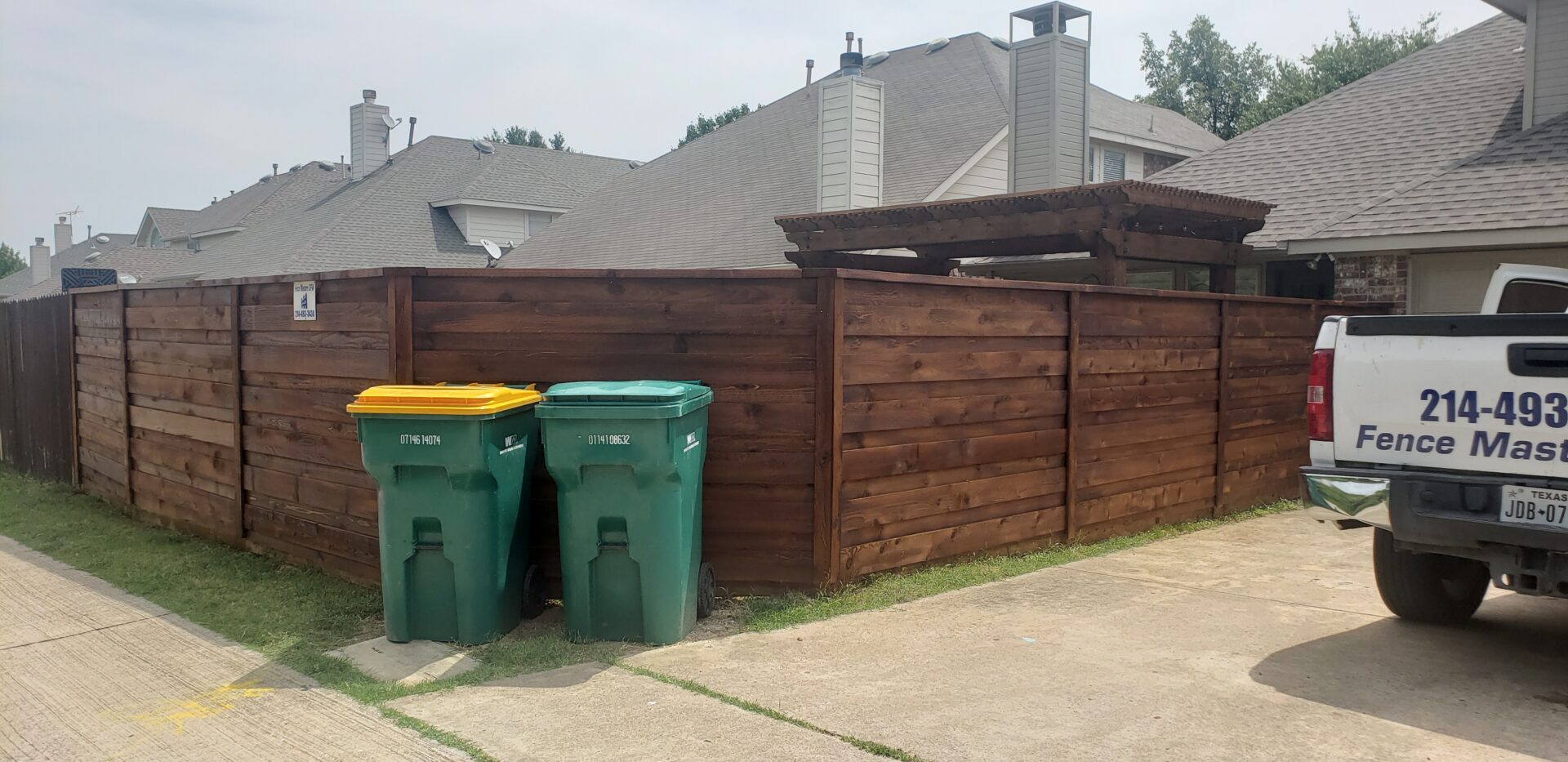 Two trash cans are next to a wooden fence.